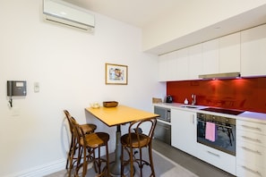 A modern kitchen with white cabinets, a wooden dining table, and a red backsplash. - ALIA, 1BDR Fitzroy Apartment (Fitzroy)