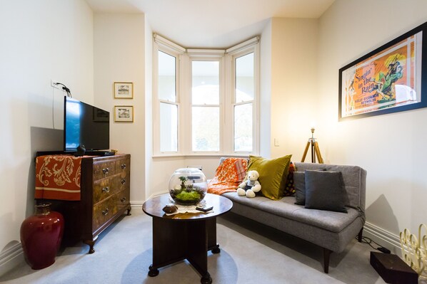 A living room with a television, a sofa, a coffee table, and a window with a view. - ALIA, 1BDR Fitzroy Apartment (Fitzroy)