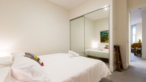 A hotel room with a large bed, a wardrobe, a mirror, and a painting on the wall. - ALIA, 1BDR Fitzroy Apartment (Fitzroy)
