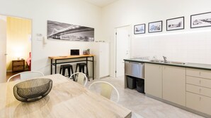 Une cuisine moderne avec un coin repas, comprenant une table en bois, des chaises, un saladier noir en treillis métallique et une grande photographie représentant un paysage urbain accrochée au mur.