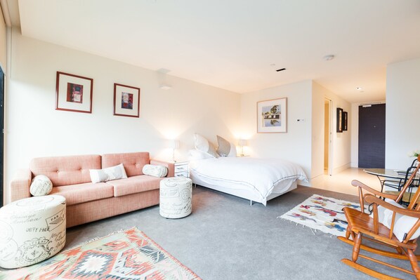 A modern bedroom with a pink sofa, a white bed, and a wooden rocking chair. - CELESTE, 1BDR East Melbourne Apartment (East Melbourne)