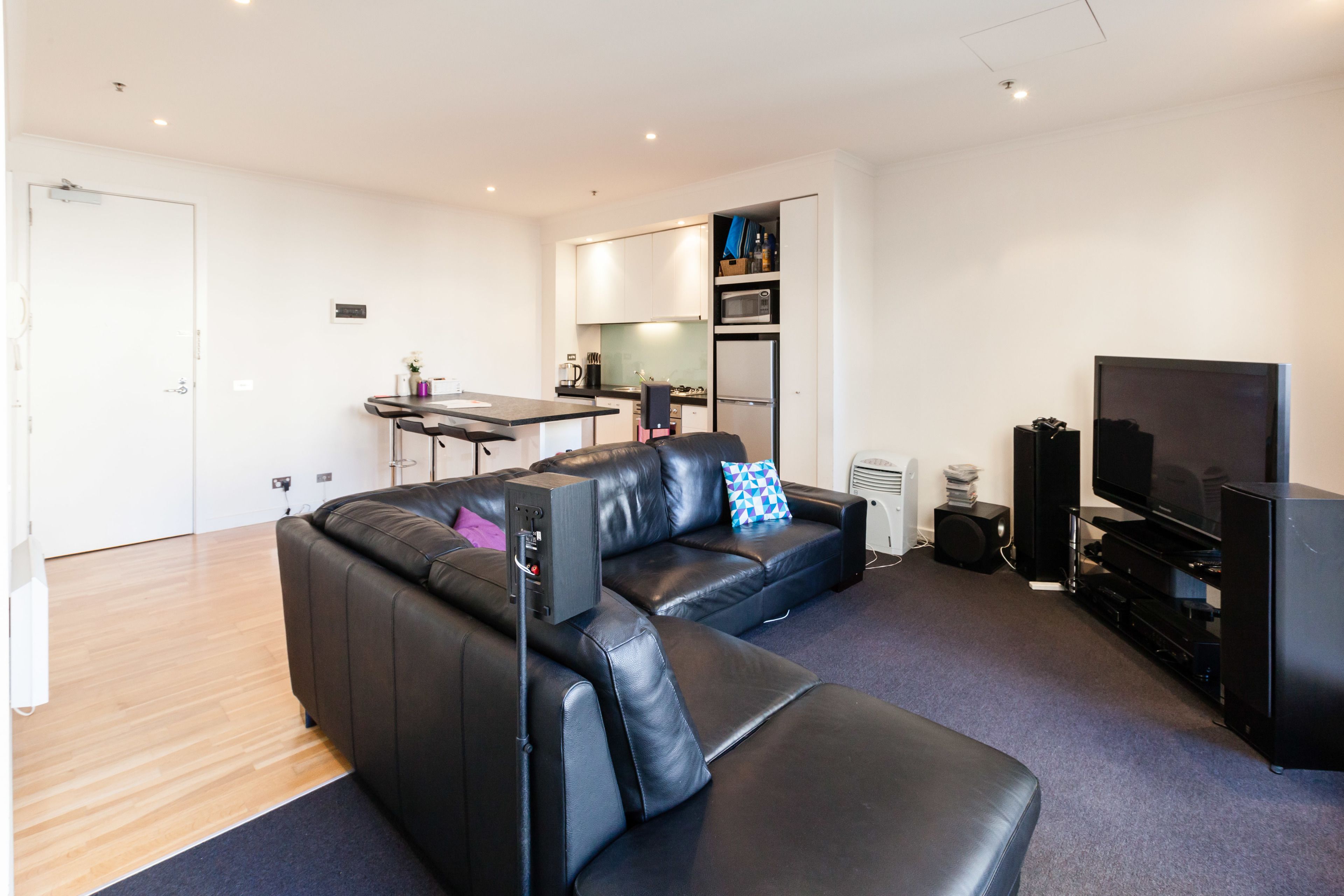 A modern living room with a sectional sofa, a flat-screen TV, and a compact kitchen area.
