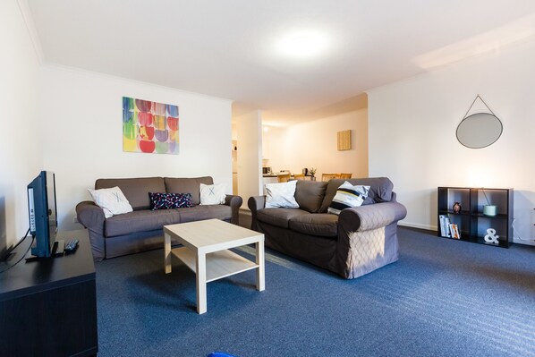 A modern living room with two sofas, a coffee table, and a TV on a stand. - DAWN, 2BDR Carlton Apartment (Carlton)