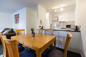 Cozy living space with a dining area and kitchenette, featuring a sofa, wooden dining table, and microwave.
