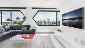A modern living room with a sectional sofa, a red coffee table, and a large TV on the wall. - ELAINE, 2BDR St.Kilda Apartment (St Kilda)