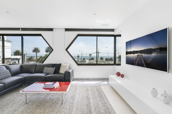 Un salon moderne avec un canapé d’angle, une table basse rouge et un grand téléviseur fixé au mur.