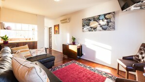 Un salon moderne avec un canapé, des fauteuils, un tapis rouge et un téléviseur à écran plat fixé au mur.