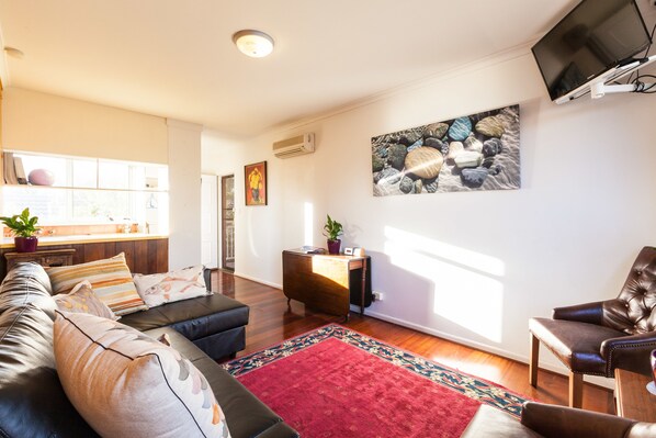 Een moderne woonkamer met een bank, fauteuils, een rood tapijt en een flatscreen televisie aan de muur.