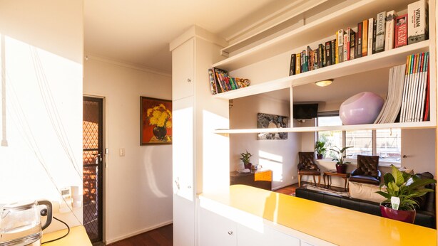 Une cuisine moderne avec des meubles blancs, un plan de travail jaune et une bibliothèque remplie de livres.