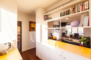 Een moderne keuken met witte kastjes, een geel aanrecht en een boekenplank vol boeken.