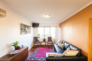 A living room with a black leather sofa, two chairs, a small table, a TV, and a window with blinds.