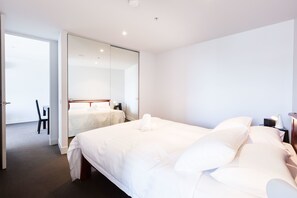 A hotel room with a large bed, a bedside table with a lamp, a chair, and a wardrobe with a mirror. - ERICA, 2BDR South Yarra Apartment (South Yarra)