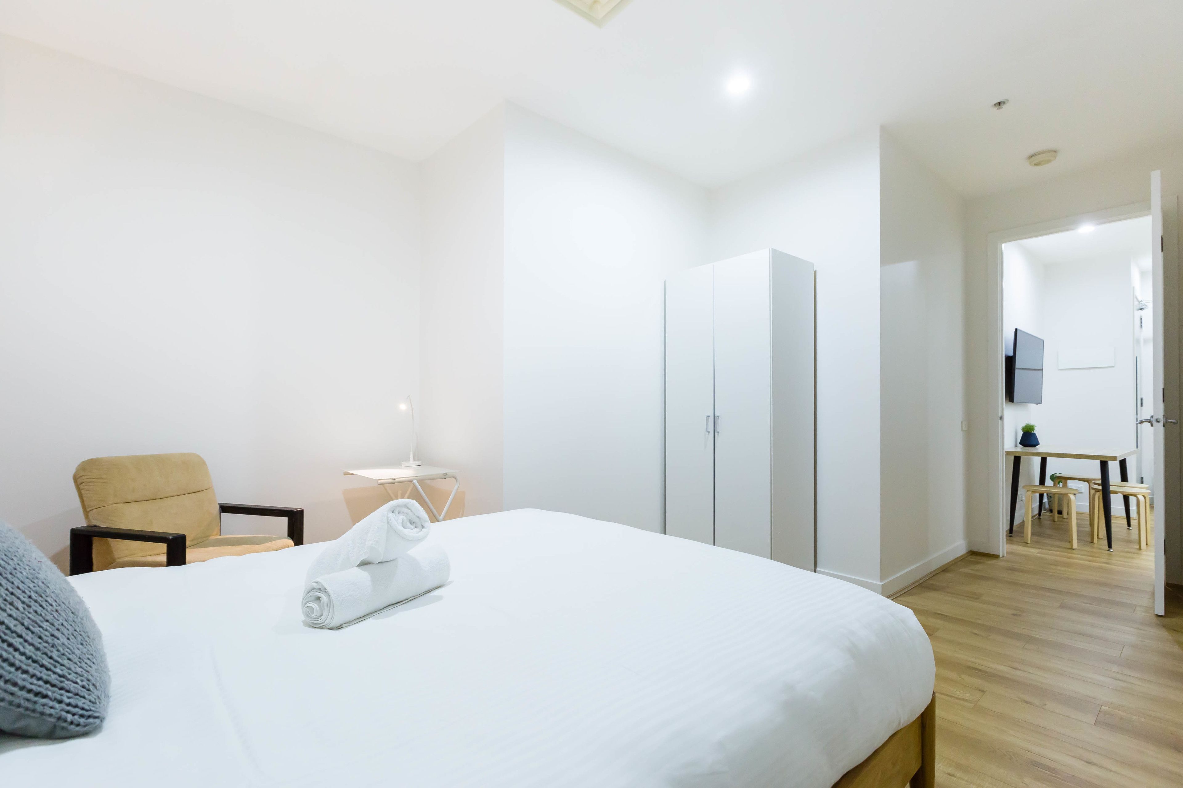 A hotel room with a large bed, a chair, a desk, and a wardrobe.