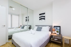 A modern hotel room with a large bed, a bedside table with a lamp, and a mirror.