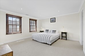 Quarto com uma cama grande, duas janelas, uma mesinha de cabeceira e um quadro na parede.