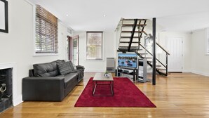 A modern living room with a fireplace, a black leather sofa, a red rug, and a staircase leading to an upper floor. - HELENA, 2BDR Fitzroy House (Fitzroy)