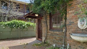 A brick house with a balcony, a stone lion sculpture, and a garden with flowers and shrubs. - HELENA, 2BDR Fitzroy House (Fitzroy)