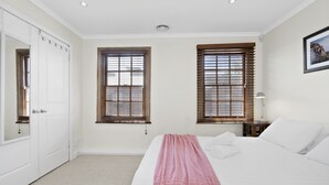 A bedroom with a bed, two windows, a nightstand, and a door. - HELENA, 2BDR Fitzroy House (Fitzroy)
