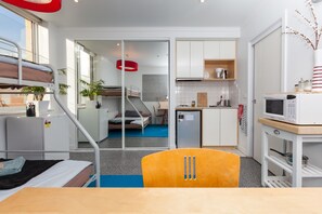 A compact hotel room with a bunk bed, kitchenette, and a small dining area.
