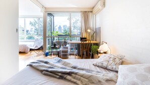 Une chambre moderne dotée d’un grand lit, d’un bureau et d’un balcon offrant une vue sur la ville.