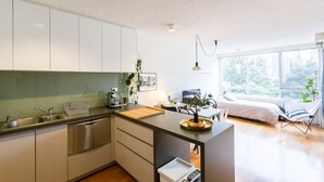 Une cuisine moderne avec un îlot central, un coin repas comprenant une table et des chaises, et une chambre avec un lit et une fenêtre.