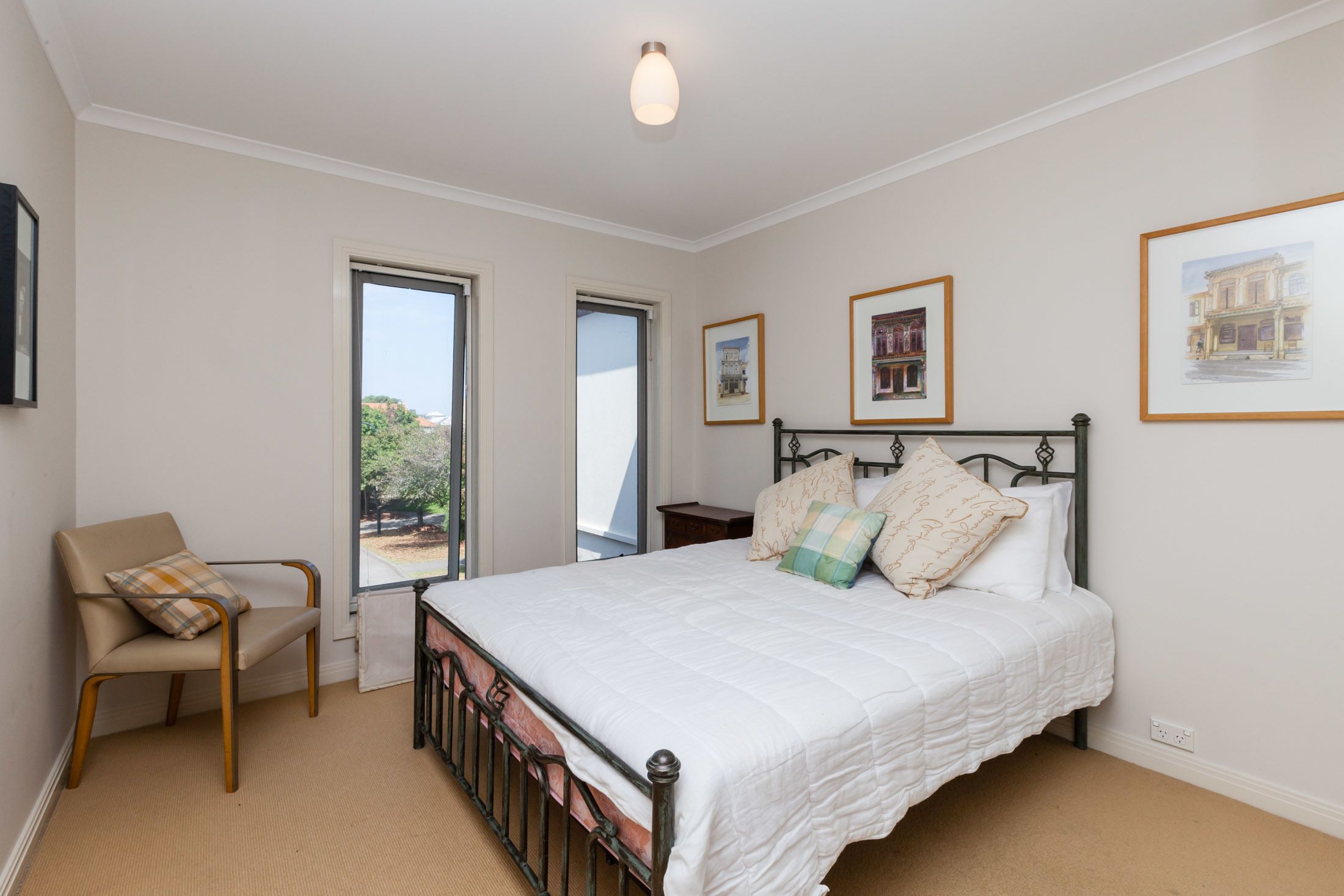 A bedroom with a bed, a chair, and large windows.