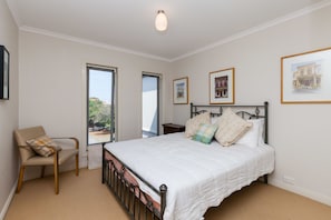 A bedroom with a bed, a chair, and large windows. - JASMINE, 2BDR Port Melbourne House (Port Melbourne)