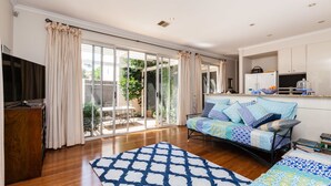 A spacious living area with a sofa set, a wooden cabinet, and a large window with curtains. - JASMINE, 2BDR Port Melbourne House (Port Melbourne)
