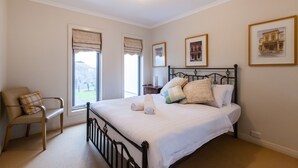 A bedroom with a bed, a chair, and two windows with blinds. - JASMINE, 2BDR Port Melbourne House (Port Melbourne)