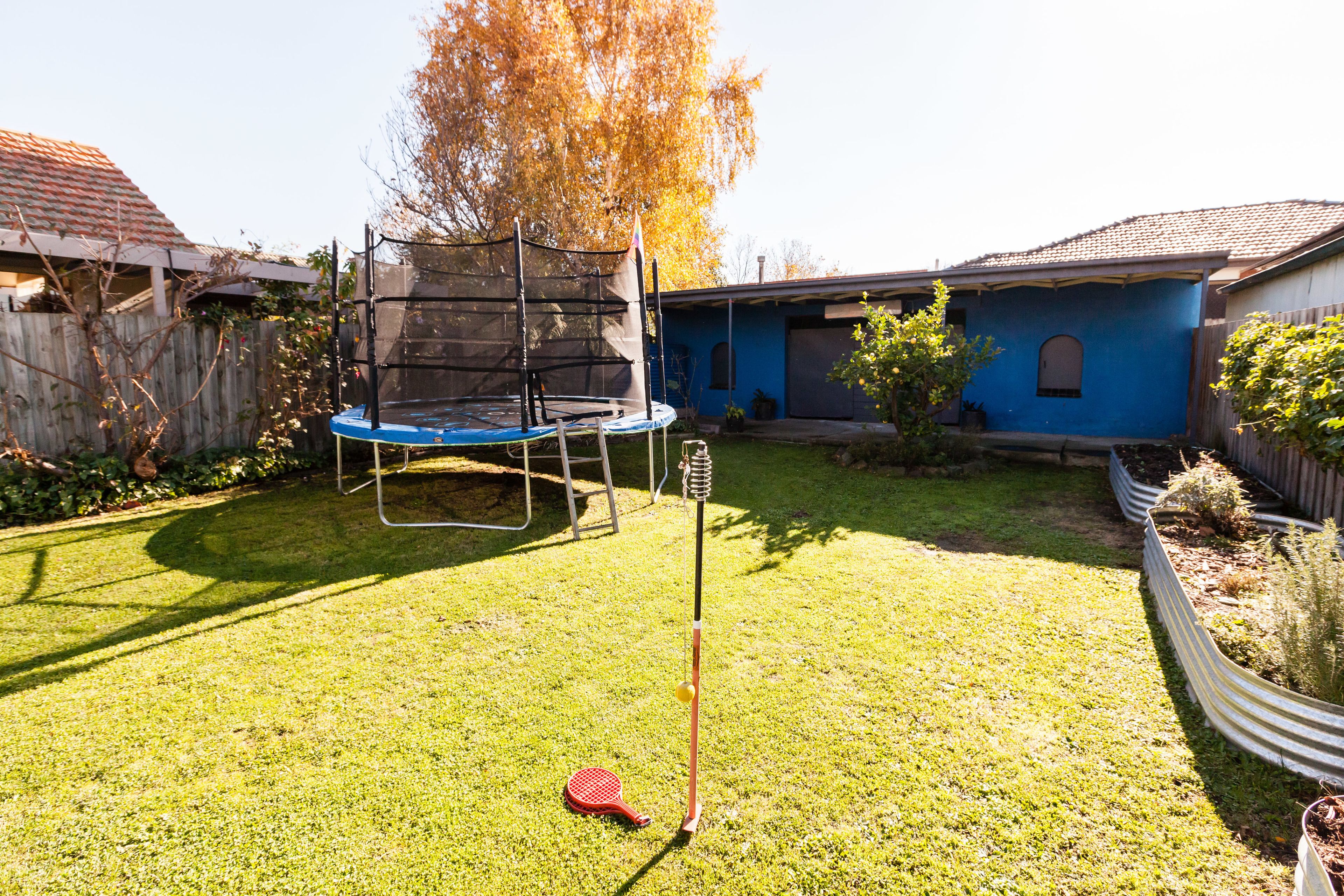 A backyard with a trampoline, a baseball tee, and a swing set.