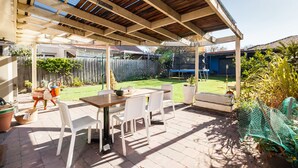 A covered patio with a table and chairs, a wooden ceiling, and a view of a backyard with a fence and greenery. - KELLY, 3BDR Northcote House (Northcote)