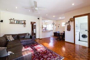 A spacious living area with a brown leather sofa, a red patterned rug, and a ceiling fan. - KELLY, 3BDR Northcote House (Northcote)