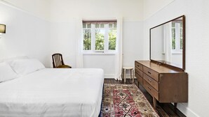 Un dormitorio con cama, cómoda de madera, una silla, ventana con cortinas y alfombra estampada.