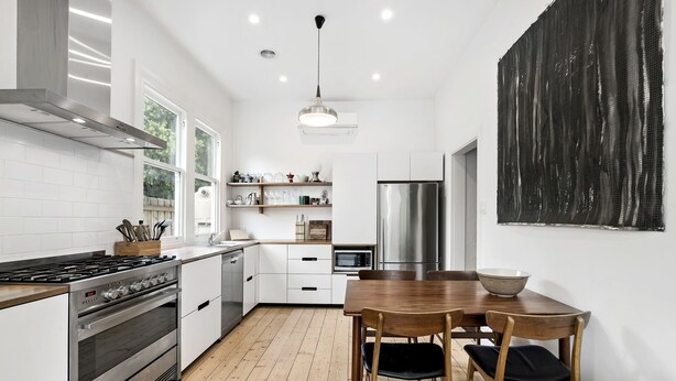 Una cocina moderna con armarios blancos, electrodomésticos de acero inoxidable y una mesa de comedor de madera con sillas.