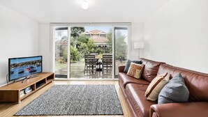 Un salón con televisor, un sofá de cuero marrón y vistas a un patio con mobiliario exterior.