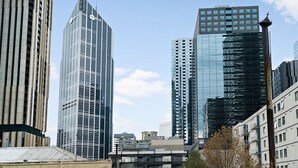 Un paisaje urbano con modernos rascacielos, incluyendo una imponente torre de cristal con un logotipo visible.