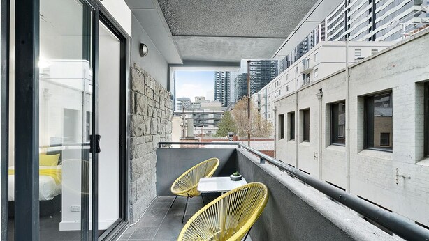 Un balcón con dos sillas amarillas y una mesita, con vistas a un paisaje urbano con edificios modernos.