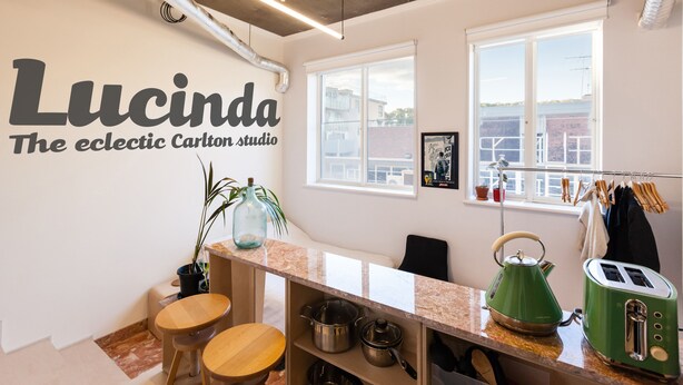 A modern kitchen with a marble countertop, a green kettle, and a toaster. There's a window with a view of buildings and a sign on the wall that reads "Lucinda The eclectic Carlton studio". - LUCINDA, Carlton Studio Apartment (Carlton)