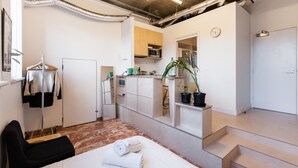 A compact hotel room with a bed, a seating area, a kitchenette, and a bathroom. - LUCINDA, Carlton Studio Apartment (Carlton)