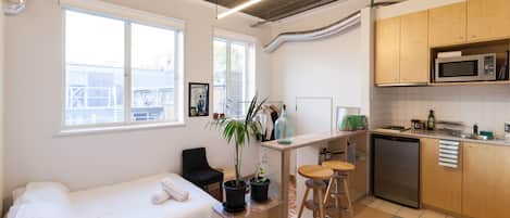 A compact room with a bed, a small kitchenette, and a window.