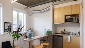 A modern kitchen with wooden cabinets, a built-in microwave, and a dishwasher. There are two stools at the counter and a potted plant. - LUCINDA, Carlton Studio Apartment (Carlton)