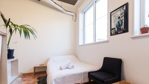 A small, neatly arranged room with a bed, a chair, a small table, and a potted plant. - LUCINDA, Carlton Studio Apartment (Carlton)