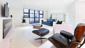 A modern living room with a flat-screen TV, a large window, a sofa, a coffee table, and a black leather chair. - MADDISON, 3BDR Port Melbourne Apartment (Port Melbourne)