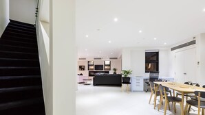 A modern kitchen with a dining area, featuring a staircase leading to an upper level. - MADDISON, 3BDR Port Melbourne Apartment (Port Melbourne)