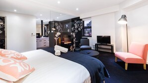 A modern hotel room with a large bed, a seating area with a TV, and a fireplace. - MADDISON, 3BDR Port Melbourne Apartment (Port Melbourne)