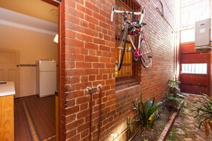 A brick wall with a bicycle rack, a refrigerator, and a small garden area with plants. - MADELINE, 1BDR Fitzroy Apartment (Fitzroy)