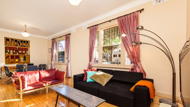 A living room with a wooden floor, a black sofa, a red leather sofa, a coffee table, and a TV stand.