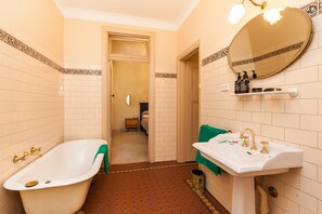 A bathroom with a bathtub, sink, and mirror. There is a towel rack and toiletries on the sink. - MADELINE, 1BDR Fitzroy Apartment (Fitzroy)