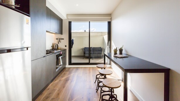 Una cocina moderna con armarios oscuros, suelo de madera y puerta corrediza de vidrio que da a un balcón con sofá.