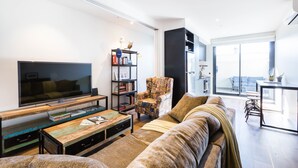Una sala de estar moderna con una televisión de pantalla plana, un sillón estampado, un sofá y una estantería.